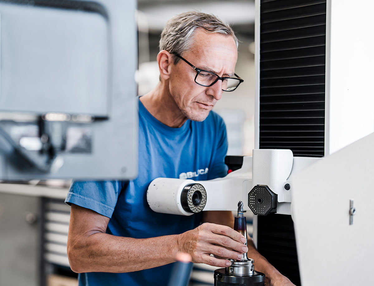 Nahaufnahme eines Biltec-Mitarbeiters, der sorgfältig eine kubische Fertigungsmaschine einstellt, um den nächsten Produktionsschritt vorzubereiten, wobei besonderer Wert auf Genauigkeit und Präzision gelegt wird.